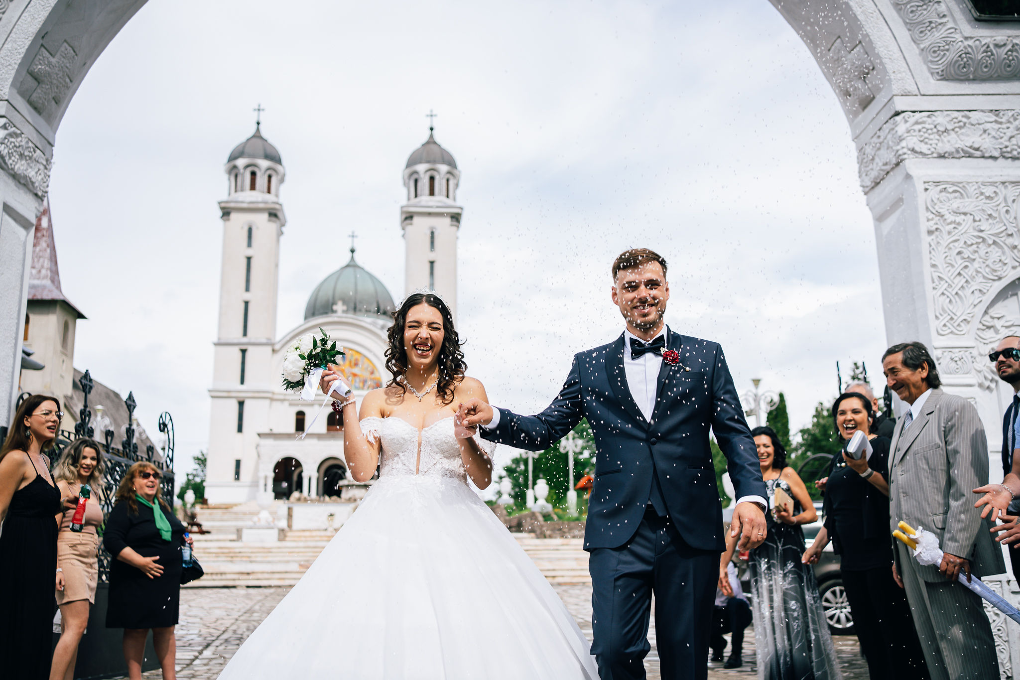 Mirii ies din curtea bisericii sub ploaia de confetti aruncate de invitați.