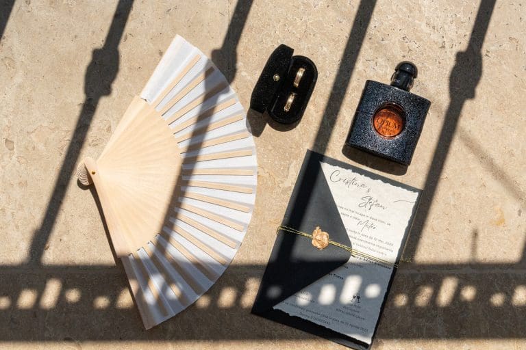Detalii de nuntă elegante fotografiate în lumină naturală: evantai, verighete, invitație și parfum