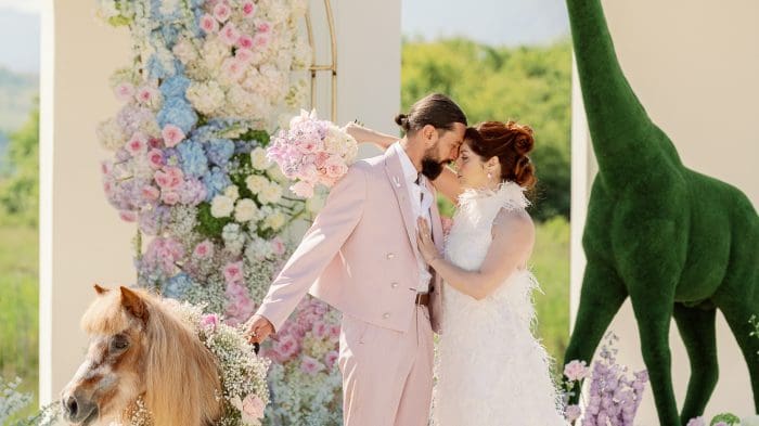 Cuplu fotografiat la styled shoot de nuntă, cu decor pastelat, ponei floral și girafă decorativă verde