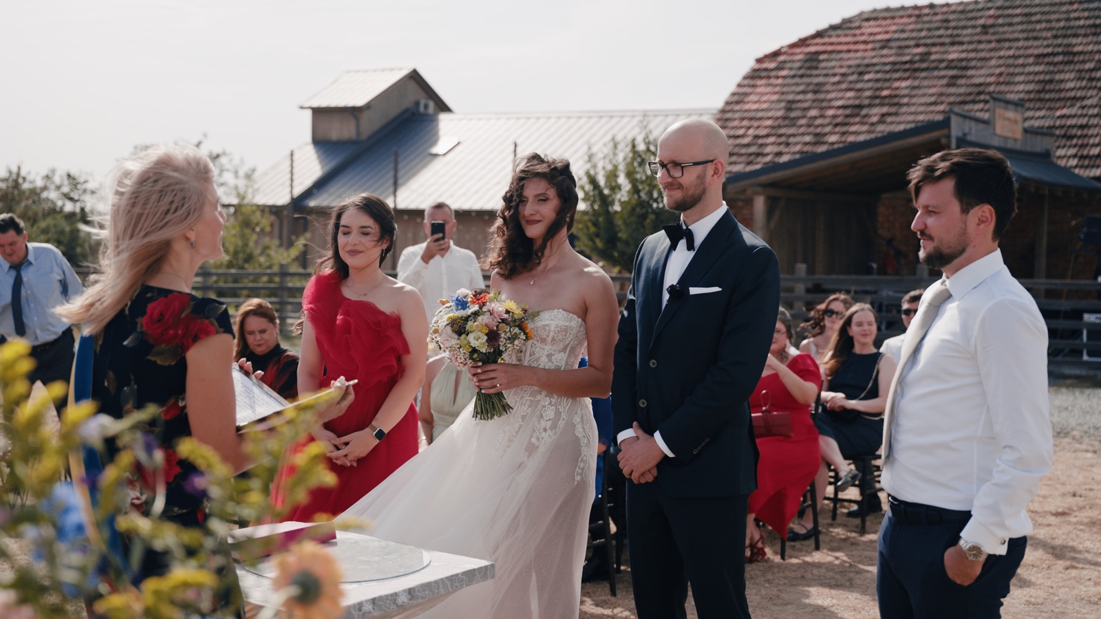 Sorin și Oana în fața ofițerului de stare civilă, cu invitații așezați în spate, pe câmp